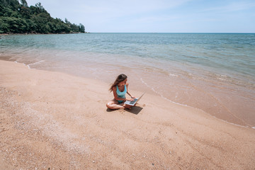 Young happy fitness yoga woman working with her laptop sitting in the beach  in Thailand , relaxing enjoy with nature