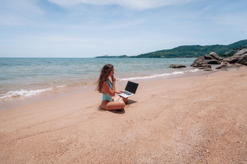 Young happy fitness yoga woman working with her laptop sitting on sitting on the sand, relaxing enjoy with nature.
