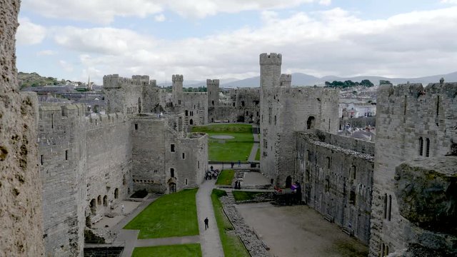 Distant unidentifiable visitors tour the courtyard at Caernarfon Castle medieval fortress in Caernarfon, Gwynedd, Wales