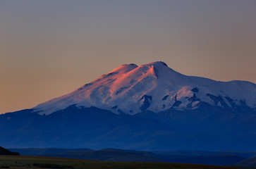 Fototapeta premium Mount Elbrus at dawn. View of the sunlit slopes of the volcano from the northwest. The North Caucasus in Russia.