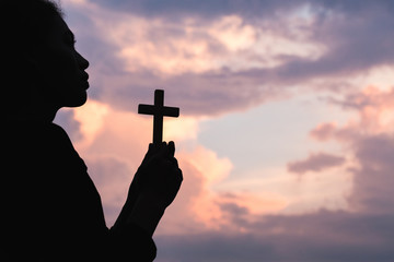 Silhouette off  woman hands holding wooden cross  on sunrise background, Crucifix, Symbol of Faith.