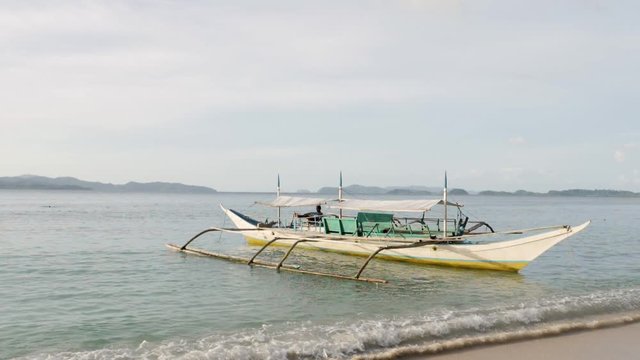 Ultra slow motion shot of traditional filipino bangka boat in white and yellow anchored in shallow clear waters early morning