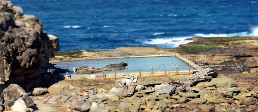 Rock pool at North Curl Curl Beach, Sydney, Australia. People Enjoying an ocean pool. Seaside ocean swimming pool with metal hand rail fencing set against calm blue water and large exposed rocks