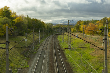 Fototapeta na wymiar paths of the turning railway in the autumn, among the yellowing trees and the autumn cloudy sky