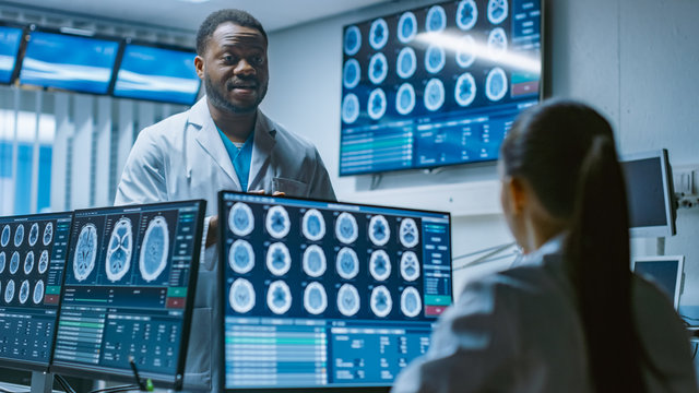 Two Medical Scientists in the Brain Research Laboratory Discussing Progress on the Neurophysiology Project. Neuroscientists Use Personal Computer with MRI, CT Scans Show Brain Images.