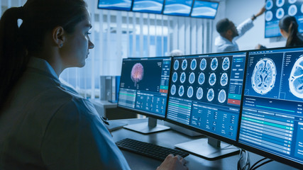 Over the Shoulder Shot of Female Medical Scientist Working with CT Brain Scan Images on a Personal Computer in Laboratory. Neurologists in Research Center Work on Brain Tumor Cure. - obrazy, fototapety, plakaty