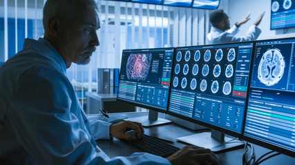Over the Shoulder Shot of Senior Medical Scientist Working with CT Brain Scan Images on a Personal...