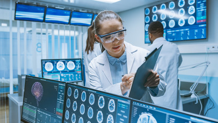 Senior Medical Scientist Consults Female Apprentice with Clipboard, He Works with CT Brain Scan Images on a Personal Computer in Laboratory. Neurologists in Research Center Work on Brain Tumor Cure. - obrazy, fototapety, plakaty