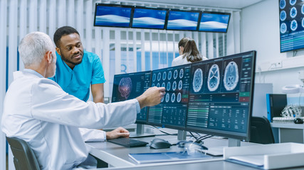 Medical Scientist and Surgeon Discussing CT / MRI Brain Scan Images on a Personal Computer in...
