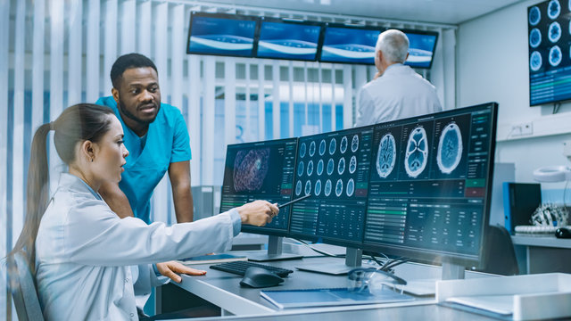 Medical Scientist and Surgeon Discussing CT Brain Scan Images on a Personal Computer in Laboratory. Neurologists / Neuroscientists in Neurological Research Center Working on a Brain Tumor Cure.