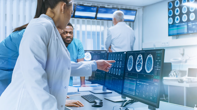 Diverse Team of Medical Scientists Solve Problems and Point at Computer Screens Showing CT, MRI Scans. Neurologists / Neuroscientists Working in Brain Research Laboratory.