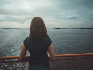 Woman on her back, observing in the distance, the statue of liberty, clinging to the railing of a ship, in New York, USA