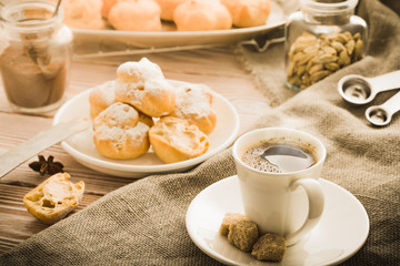 Cup of hot black coffee with home made profiteroles on a rustic wooden table.