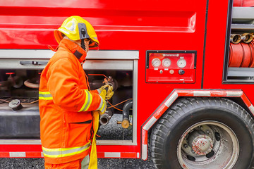 Naklejka premium Firefighter holding water hose near the truck with equipment at fire station