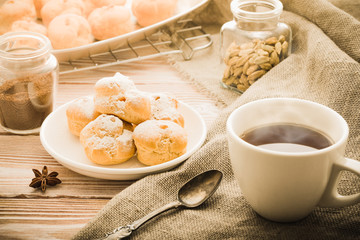 Cup of black tea with home made profiteroles on a rustic wooden table.