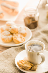 Cup of hot black coffee with home made profiteroles on a rustic wooden table.