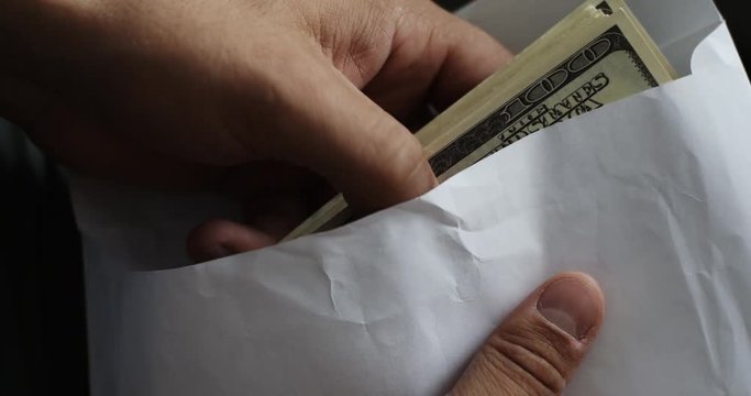 Closeup shot of man looks into the envelope which is pack of 100 dollar bills