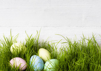 Easter eggs laying in green grass near the old white wooden wall background