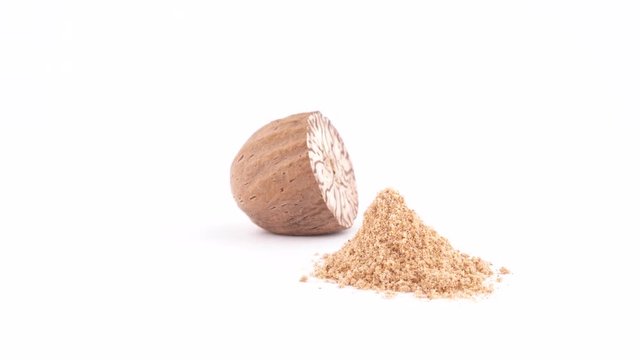 One half of blanched macadamia nut with nutmeg powder. Slowly rotating on the turntable isolated on the white background. Close up. Macro.