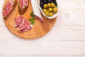 Salami and bread on white wooden background. Top view. Copy space