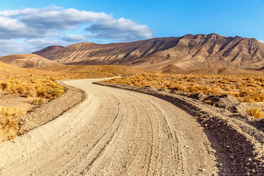 Winding rural Dirty Road Across Volcanic Landscape in Fuerteventura at Golden Hour