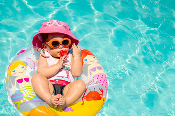 Adorable Baby Girl Wearing Hat and Sunglasses Sucking A Binky On Blue Water