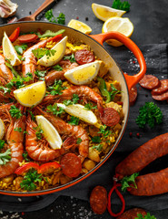 Traditional paella in the fry pan with chicken, prawns, spicy chorizo, lemon and glass of white wine.