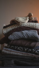 a stack of knitted warm cozy clothes, on a chair by the white wall. autumn concept.