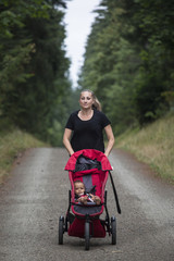 Attractive Woman running on a trail pushing her baby stroller outdoors. Vertical image of a fit female working out while being an active mom