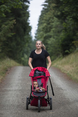 Attractive Woman running on a trail pushing her baby stroller outdoors. Vertical image of a fit...