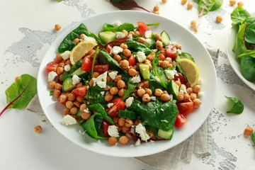Chickpeas Salad with cucumber, tomatoes, feta cheese and green mix in a white plate. healthy food.