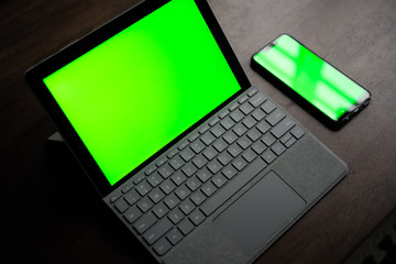 A Computer Tablet and ultra-slim smartphone with green screen/chroma key on brown table