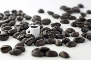 Fototapeta na wymiar A tiny miniature cup surrounded by coffee beans isolated on white