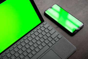 A Computer Tablet and ultra-slim smartphone with green screen/chroma key on brown table