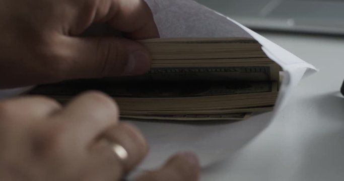 Closeup shot of man looks into the envelope which is pack of 100 dollar bills