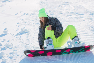 Snowboarder woman sitting and fasten board on legs