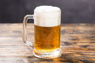 Mug of cold pale beer placed on a rustic wooden table with copy space.