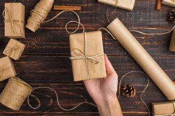 Women's hands hold a gift of craft paper. Against the background of dried orange, cinnamon, pine cones, anise on a wooden table.