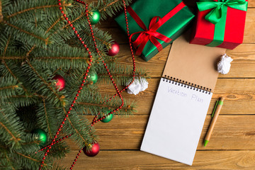 Green red gifts and notepad under the tree, on the table, against the wood background. The concept of Christmas and New Year.