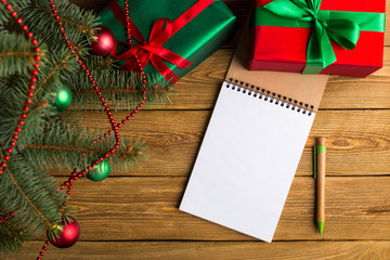 Green red gifts and notepad under the tree, on the table, against the wood background. The concept of Christmas and New Year.