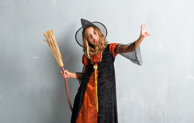 Obraz premium Little girl dressed as a witch and holding a broom for halloween holidays making victory gesture