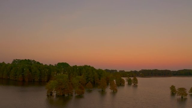 High altitude video of a beautiful sunset at stumpy lake Virginia with birds flying amidst the trees