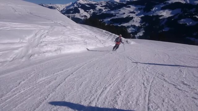 Rear view of man skiing on a narrow slope in the Alps. Mountains in the background. Sunny day.