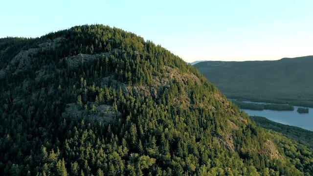 Aerial drone shot orbiting around the peak of Bore Mountian covered in thick green trees above the forest and lakes fn the Maine wilderness.