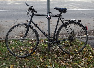 Black Mountain City Multi Speed Road Bike Cycle Bicycle With Anti Theft Lock Parked On The Green Grass With Leafs Behind Asphalt 