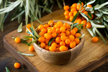 Fresh sea buckthorn berries in a wooden bowl on a rustic background.
