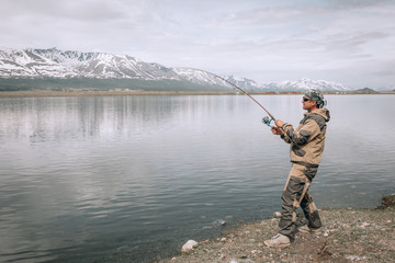 The guy fishing on the shore of a mountain lake . Reflection of mountains in water