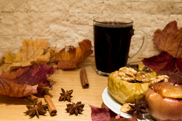 Mulled red wine with healthy dessert, baked apples with honey and nuts. Decorated with dried colorful leaves, cinnamon rolls and anise stars. Close up.