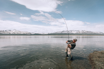 The guy fishing on the shore of a mountain lake . Reflection of mountains in water