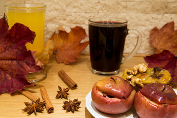 Hot mulled wine and baked apples with spices, walnuts, cinnamon sticka, cloves and anise stars, autumn scene with colorful dried leaves on bricks wall background. Hot red wine in glass cup.